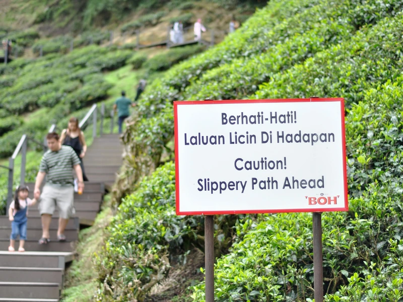 A slippery path caution sign at BOH Tea Plantation, highlighting the steep terrain and why booking our safe private car is essential for your Cameron Highlands day trip.