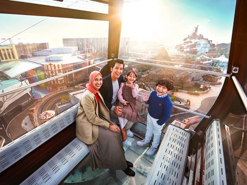 A family enjoying the rainforest view from the Awana SkyWay glass floor gondola, a thrilling attraction made luggage-free with your Genting Highlands day trip private car service.