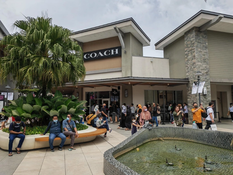Shoppers resting by the fountain outside the popular Coach boutique at Genting Highlands Premium Outlets, securely storing their luxury purchases in their Genting Highlands day trip private car.