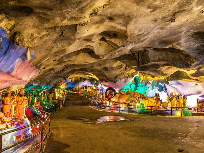 Colourful Hindu mythology statues illuminated inside the stunning limestone Batu Caves, a fascinating highlight of your Kuala Lumpur day trip private car tour.