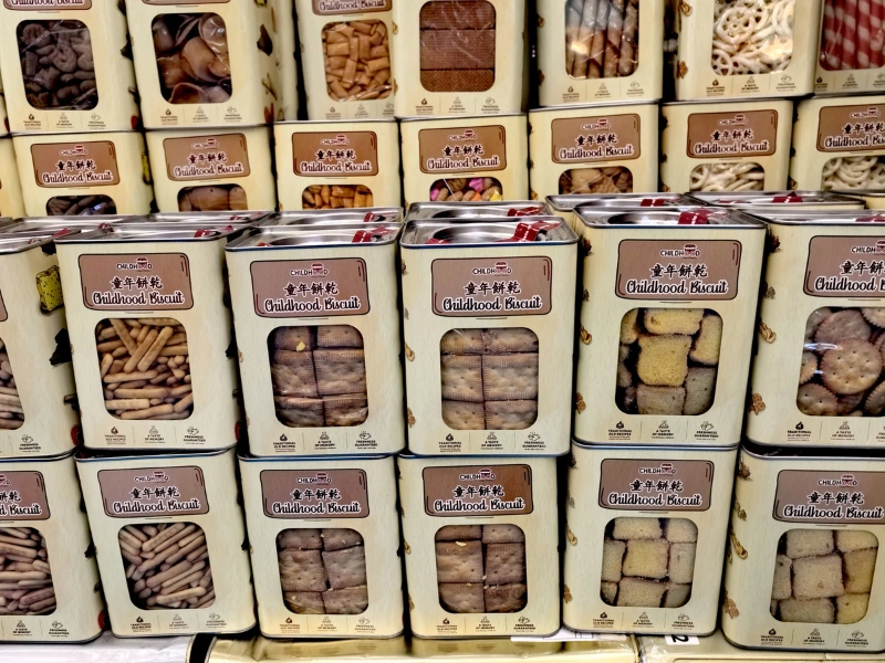 Stacks of traditional Childhood Biscuit tin cans near Jalan Alor, a nostalgic souvenir shopping stop made effortless with your Kuala Lumpur day trip private car.
