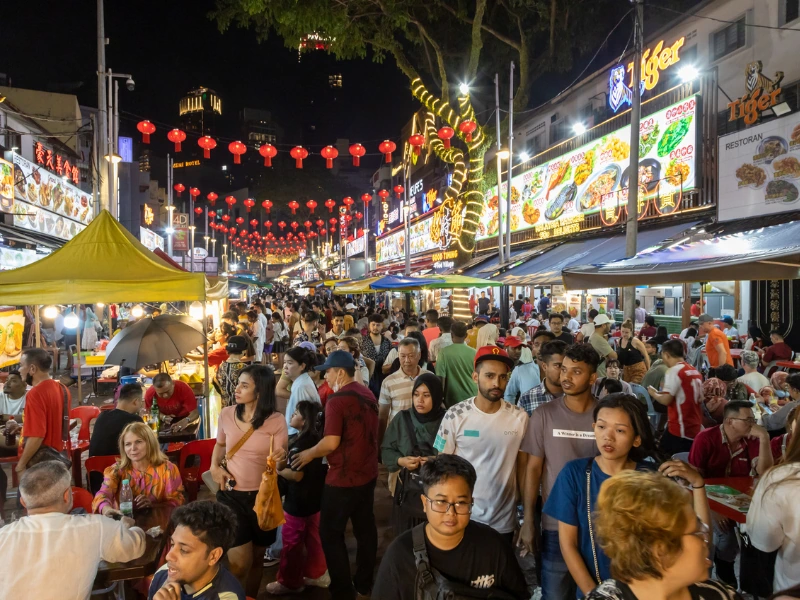 A bustling crowd enjoying street food under red lanterns at the famous Jalan Alor night market, a delicious culinary stop effortlessly managed by your Kuala Lumpur day trip private car service.