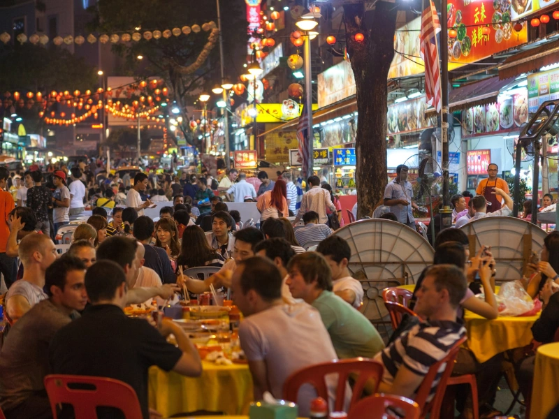 Crowds enjoying local seafood and street food at vibrant outdoor dining tables in Jalan Alor, a lively evening stop perfectly complemented by your Kuala Lumpur day trip private car service.