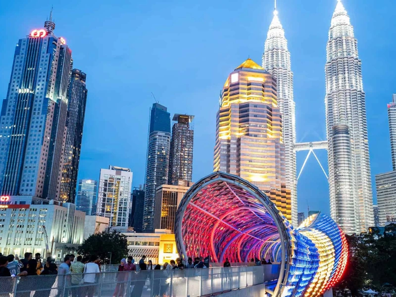 The illuminated Saloma Link bridge with the iconic Petronas Twin Towers in the background at dusk, a spectacular double-landmark view easily reached on your Kuala Lumpur day trip private car tour.
