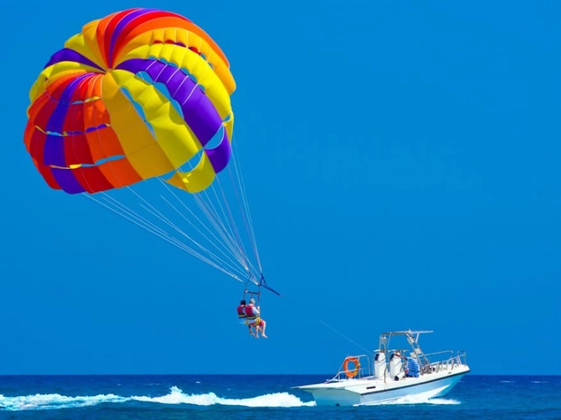 Tourists experiencing thrilling parasailing over Batu Ferringhi beach, an exciting water sport perfectly followed by a safe and restful ride in our Penang Day Trip private car.