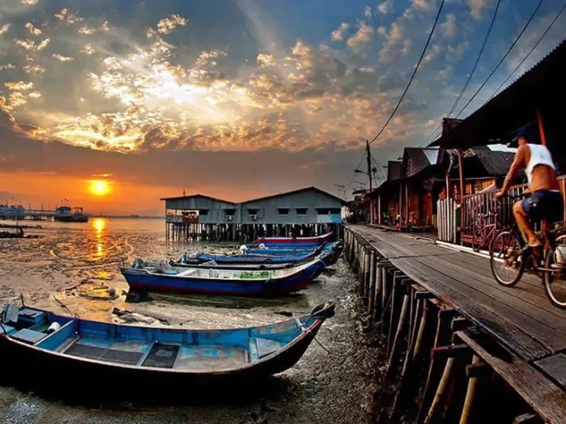 The stunning sunset view over the wooden stilt houses at Chew Jetty, a perfect evening moment on your Penang Day Trip before a relaxing ride back in our private car.