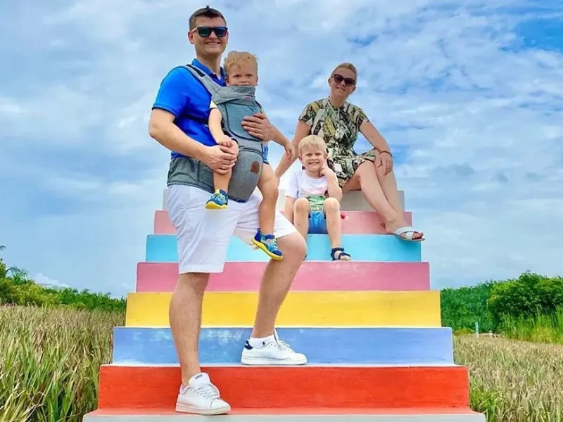 A happy family posing on the colourful rainbow stairs at Sky Ladder Pineapple Farm, a picture-perfect stop easily included in your Port Dickson day trip private car itinerary.