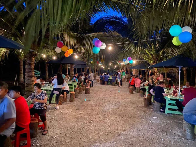Families enjoying a unique evening dining experience under the fairy lights at Sekinchan Coconut Farm, a beautiful moment made possible by the flexible schedule of your Sekinchan day trip private car.