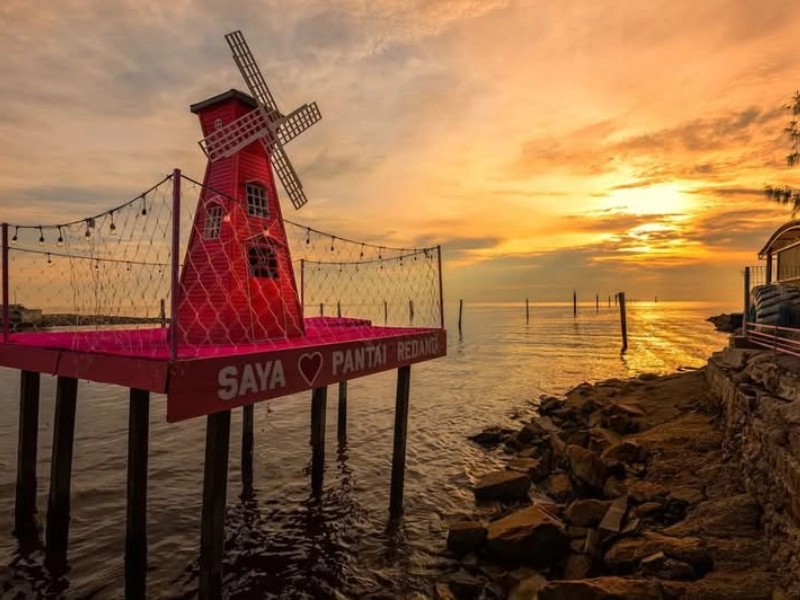 The vibrant red windmill at Pantai Redang during a breathtaking sunset, a perfect photo destination to visit at your own pace with our customized Sekinchan day trip private car itinerary.