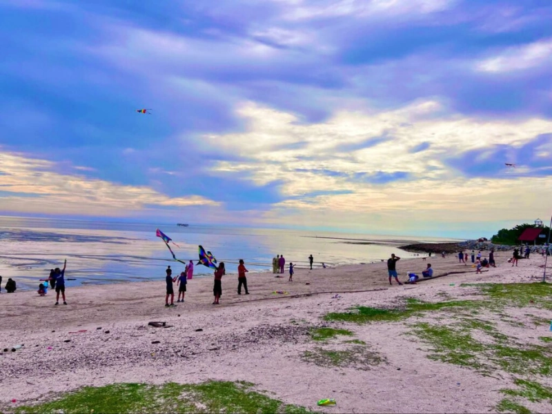 Families flying kites at Pantai Redang during a beautiful sunset, a relaxing activity you can stay for when using our flexible Sekinchan day trip private car service.
